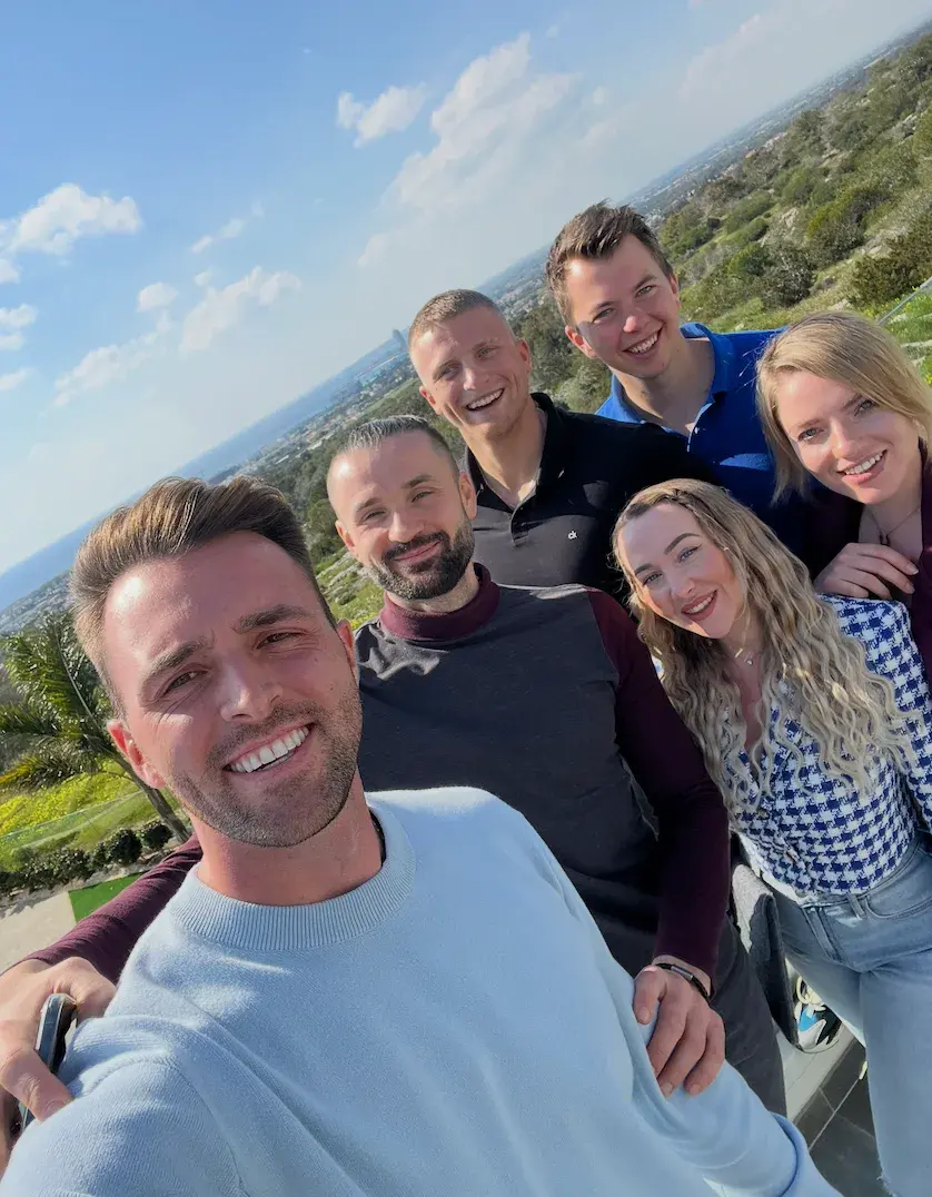 Selfie von Kevin mit fünf Klientinnen und Klienten vor Meer und Landschaft